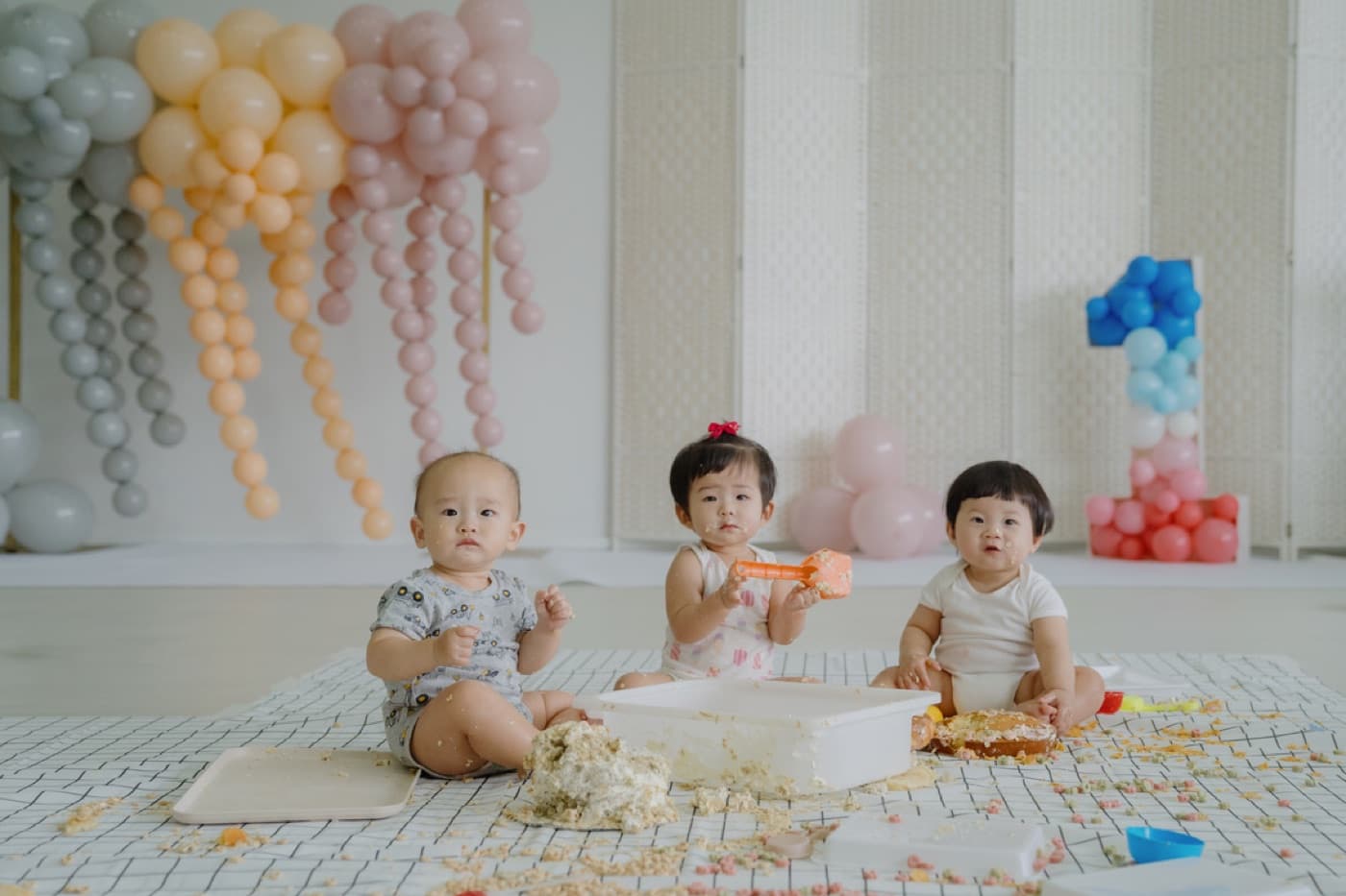 Three babies in soft pastel outfits celebrating their milestone birthday together at OurSecondHome.