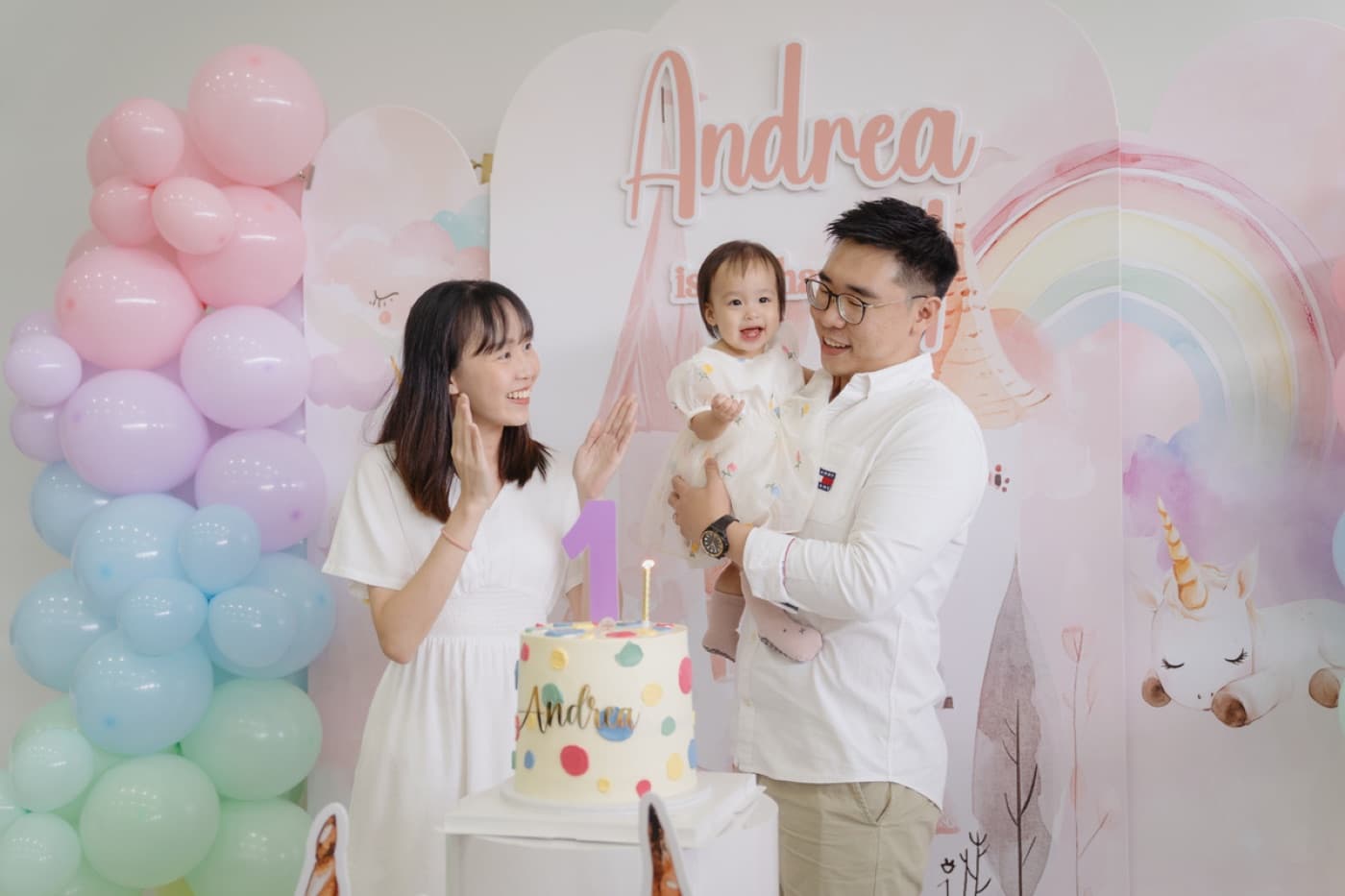 A family celebrating their little one in front of a soft pastel rainbow balloon backdrop at OurSecondHome